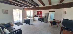 A modern living room with a sofa, a TV, and a kitchen area with a fridge, stove, and shelves. - Maison les Gastinières, surrounded by nature and near the châteaux of the Loire Valley (Fontaine Guerin)