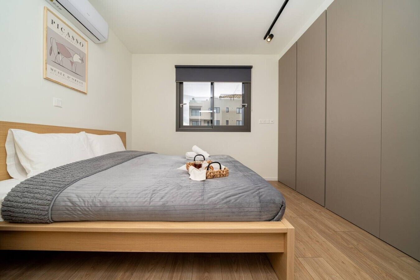 A modern bedroom with a bed, a window, a wardrobe, and a framed artwork on the wall.