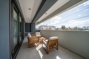 A balcony with a seating area, a glass door, and a view of buildings.
