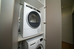 A compact laundry room with two stacked washing machines, a control panel, and a door.
