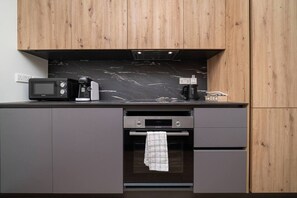 A kitchen with a microwave, coffee maker, and toaster on the counter, a small oven, and grey cabinets.