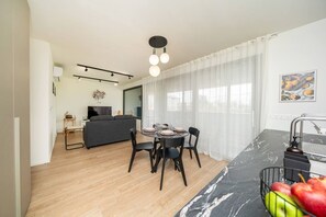 A modern apartment with a dining area, a sofa, a TV, and a kitchen with a marble countertop.