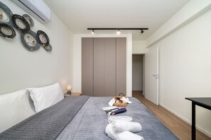 A modern hotel room with a bed, bedside table, wall art, and a wardrobe.