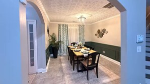 A dining area with a table set for four, a potted plant, patterned curtains, and a decorative wall piece. - Near ATL & Stone Mountain/ Sleeps 12/  King Suite (Loganville)