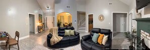 Uma sala de estar ampla com um sofá de couro preto, uma área de jantar com mesa e cadeiras, e uma escadaria que leva a outro andar.