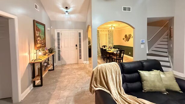 A modern living room with a black sofa, a dining area with a table and chairs, a staircase, and a hallway leading to a door. - Near ATL & Stone Mountain/ Sleeps 12/  King Suite (Loganville)