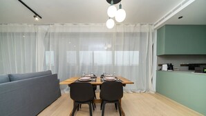 A modern dining area with a wooden table set for two, a grey sofa, and a kitchen in the background. - Amazing new 2 bedroom flat near casino beach mall (Limassol)
