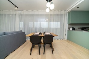 Ein moderner Essbereich mit einem Holztisch, gedeckt für zwei Personen, einer grauen Couch und einer Küche im Hintergrund.