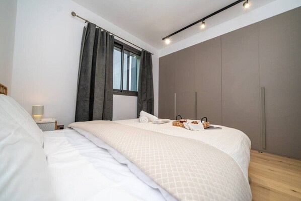 A modern bedroom with a large bed, a bedside table with a lamp, a window with curtains, and a wardrobe.