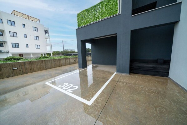 Un bâtiment moderne avec un sol mouillé, un numéro « 302 » indiquant l’emplacement, et une plante verte sur le niveau supérieur.