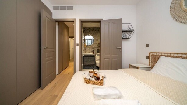 A bedroom with a bed, a bedside table, a mirror, and a bathroom visible through an open door. - Amazing new 2 bedroom flat near casino beach mall (Limassol)