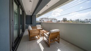 A balcony with a seating area, a glass door, and a view of buildings. - Amazing new 2 bedroom flat near casino beach mall (Limassol)