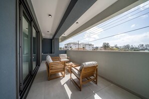 Ein Balkon mit Sitzgelegenheit, einer Glastür und Blick auf Gebäude.