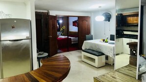 A compact kitchen with a refrigerator, a wooden dining table, a bench, and a small kitchenette area. - Cozy apartment in Itagüí | Wi-Fi | 2 bathrooms | Near Medellín (Itagüí)