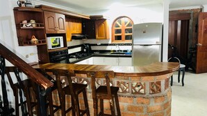 A kitchen with a central island, wooden chairs, a microwave, and a refrigerator. - Cozy apartment in Itagüí | Wi-Fi | 2 bathrooms | Near Medellín (Itagüí)