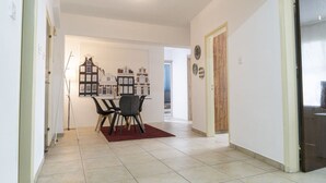 Un couloir avec un coin repas comprenant une table et des chaises, un sol carrelé et une porte donnant sur une autre pièce.