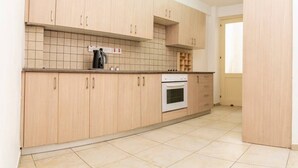 Une cuisine avec des meubles de couleur bois clair, un pare-feu en carreaux, une cuisinière et une machine à café.