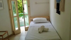 Un lit simple avec du linge de lit blanc, une tête de lit en bois et une paire de serviettes enroulées posées sur le lit.