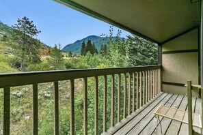 Een houten balkon met een metalen hekwerk met uitzicht op een bergachtig landschap.