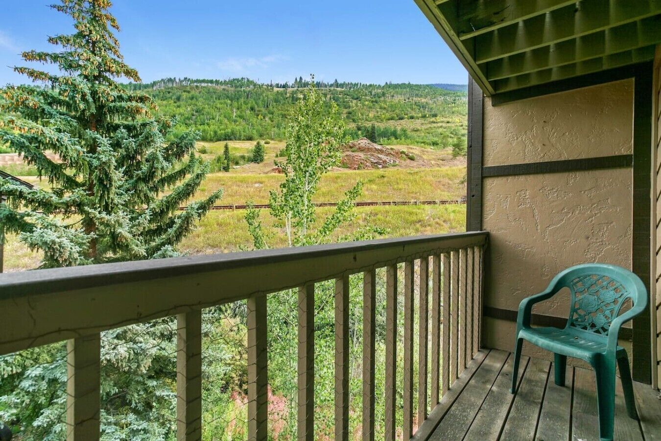 A balcony with a view of a forested landscape and a chair.