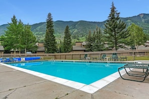 Une piscine entourée de chaises longues et délimitée par une clôture en bois, avec des montagnes en toile de fond.