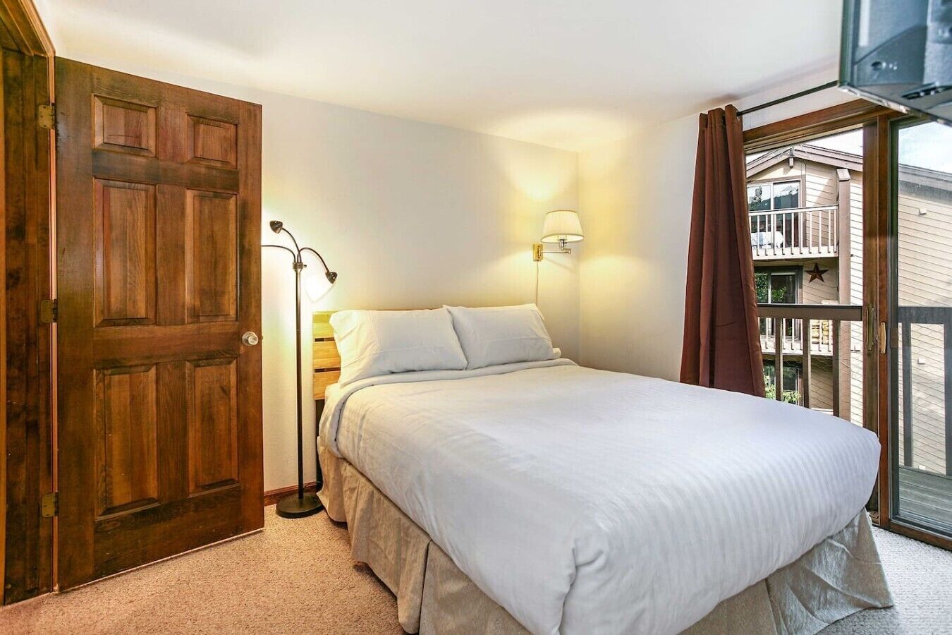 Une chambre à coucher avec un lit, une table de chevet, une lampe, une porte en bois et une vue sur le balcon.