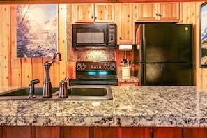 Une cuisine avec des meubles en bois, un plan de travail en granit, une cuisinière, un four à micro-ondes et un réfrigérateur.