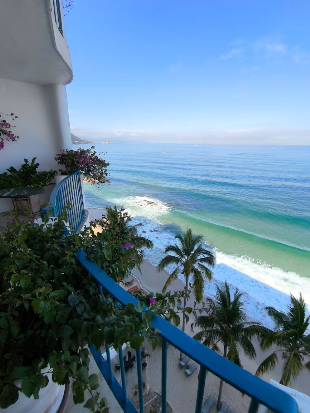 Ein Balkon mit Blick auf das Meer, eine Palme und ein blaues Geländer.