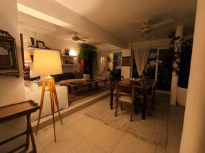 Ein Wohnzimmer mit einer Couch, einem Couchtisch, einem Esstisch, Stühlen, einer Lampe, Deckenventilator und einer Pflanze.