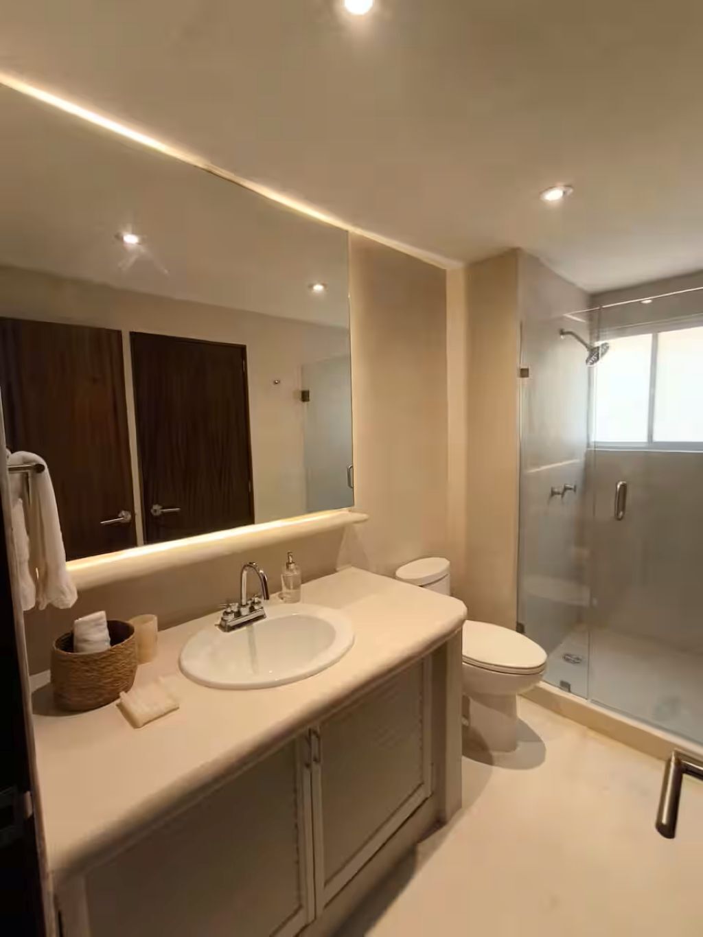 Une salle de bain moderne avec une douche à parois de verre, un grand miroir et un lavabo blanc.
