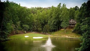 A golf course with a pond, a fountain, and a house in the background. - Duffers Delight at Rumbling Bald (Lake Lure)