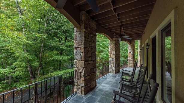 A covered porch with stone pillars, a railing, and benches. - Duffers Delight at Rumbling Bald (Lake Lure)