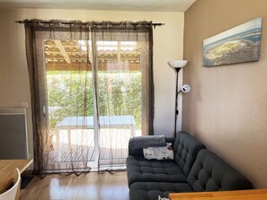 A room with a sliding glass door, a dark-colored sofa, a floor lamp, and a painting on the wall.