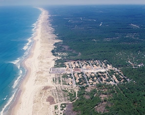An aerial view of a coastal area with a beach, residential buildings, and surrounding forest.