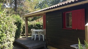 A small wooden building with a red window and a covered patio area with a table and chairs.