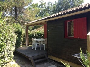 A small wooden building with a red window and a covered patio area with a table and chairs.
