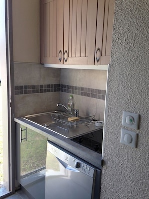A compact kitchen with a built-in dishwasher, a stainless steel sink, and a tiled backsplash.