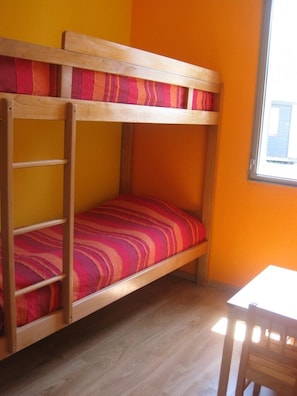 A bunk bed with a striped red and pink mattress, wooden frame, and a small table with a chair.