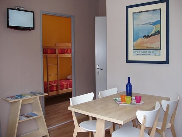 A room with a bunk bed, a table with chairs, a television, and a framed picture on the wall.