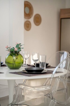 Une table à manger entourée de chaises en verre transparent, un vase vert contenant des fleurs et quelques verres à vin vides.