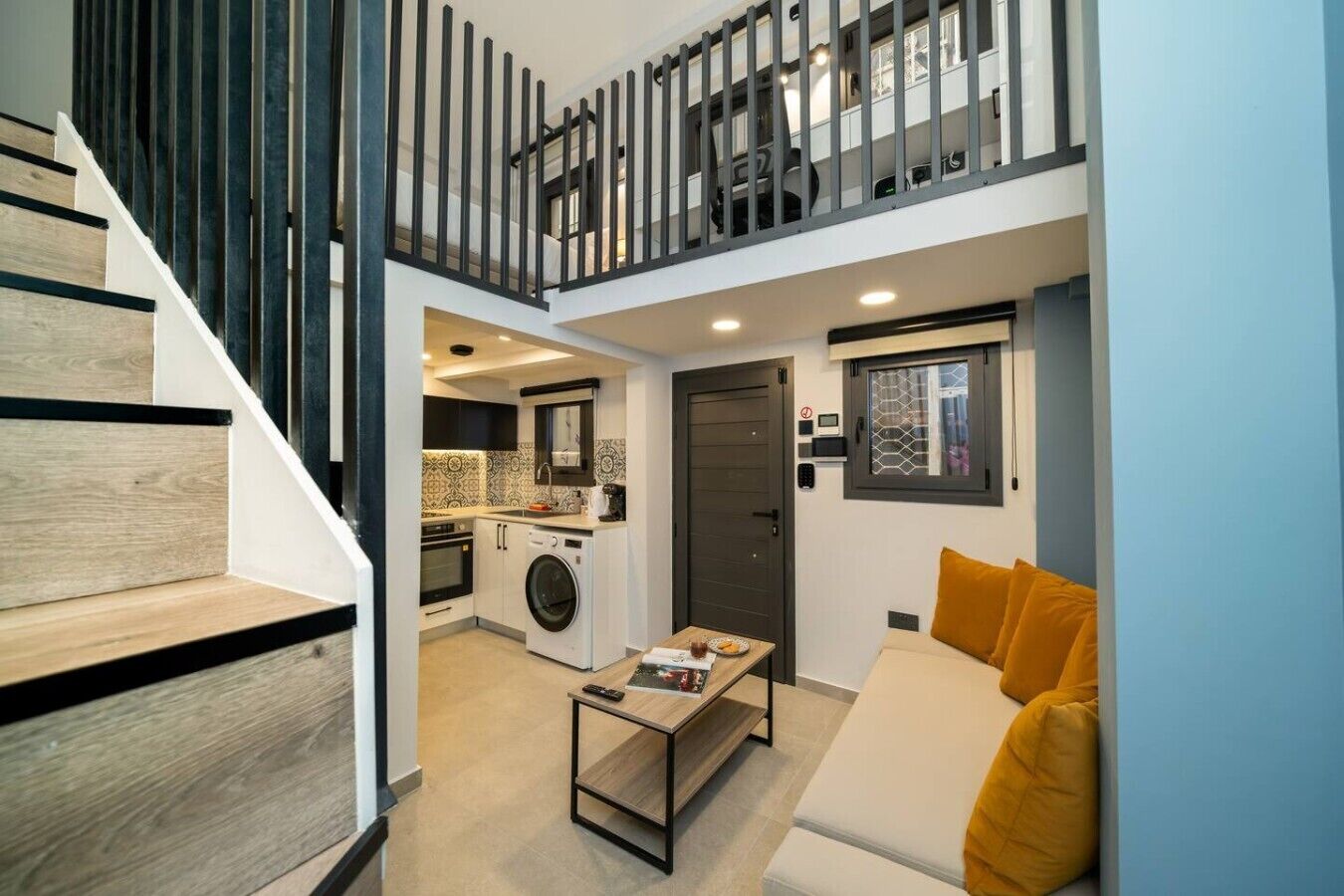 Un apartamento pequeño con escalera, una kitchenette, un área de estar con sofá y una pequeña mesa de comedor.