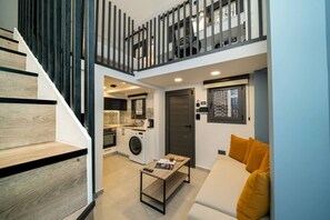 A compact apartment with a staircase, a kitchenette, a living area with a sofa, and a small dining table. - New luxury studio in historic center (Limassol)