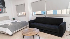 Ein modernes Zimmer mit einem Bett, einer schwarzen Schlafcouch und einem runden Holztisch.