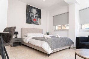 A modern bedroom with a bed, a desk, a chair, and a large window. - Modern studio in historic center (Limassol)