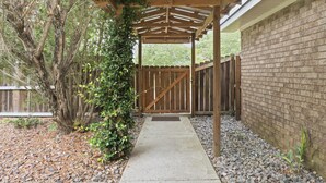 Ein überdachter Patio-Bereich mit einem Betonweg, der zu einem hölzernen Tor führt, umgeben von einer Ziegelmauer und einem Holzzaun.