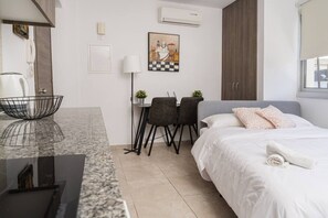 Une chambre d’hôtel moderne équipée d’un lit, d’un bureau, de deux chaises, d’une petite table, d’une lampe et d’un tableau au mur.