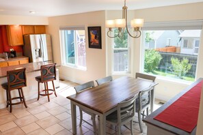 Una cocina con comedor, sillas de madera, una mesa, un refrigerador y una ventana con vista a un patio trasero.