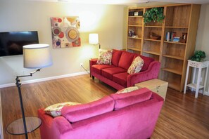 Ein Wohnzimmer mit einem roten Sofa, einem Fernseher, einer Lampe und einem Bücherregal.