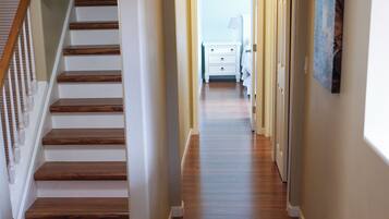 Un couloir doté d’un plancher en bois, d’un escalier et d’une porte donnant sur une chambre à coucher.