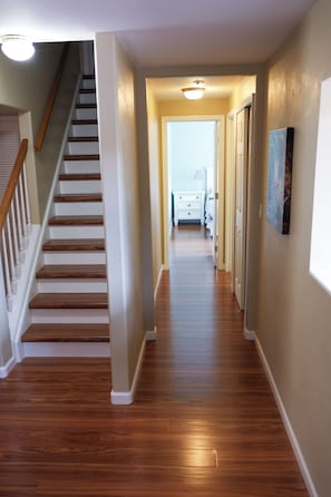 Un pasillo con suelo de madera, una escalera y una puerta que da a un dormitorio.